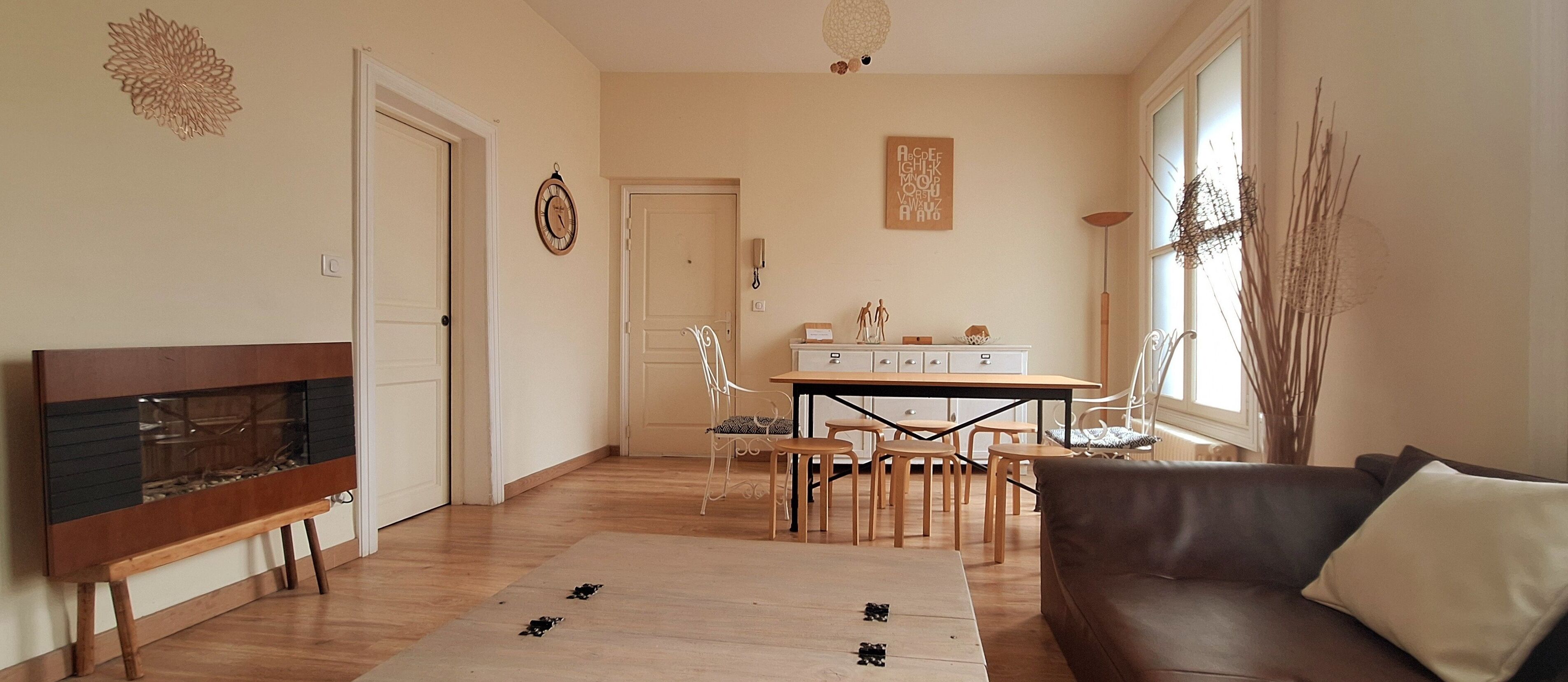 Una sala de estar con un sofá de cuero marrón, una mesa de centro de madera y una zona de comedor con mesa y sillas blancas.
