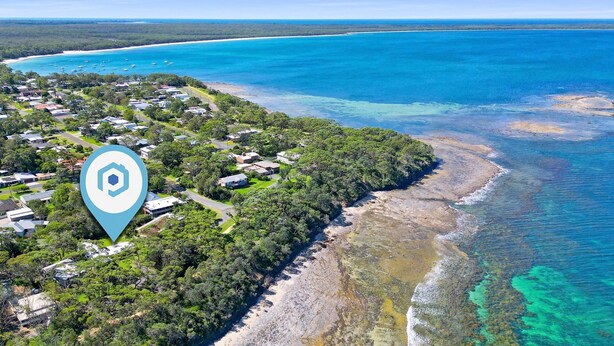 Vista aérea de una zona costera con un conjunto de casas rodeadas de vegetación exuberante y un mar azul cristalino.