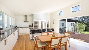 Una cocina moderna con una isla central, un comedor con sillas de madera y vistas a un jardín trasero a través de un ventanal corredero.