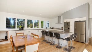 Una cocina moderna con una isla central, taburetes de bar, una mesa de comedor con sillas y un refrigerador grande.