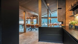 A modern kitchen with a large island, dark cabinetry, and a view of the outdoors.