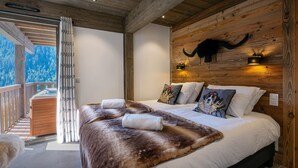 A bedroom with a large bed, wooden ceiling, and a mountain view.