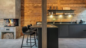 A modern kitchen with a built-in fireplace, wooden wall paneling, and a bar area with stools.
