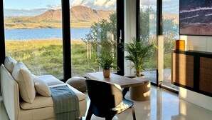 Ein modernes Wohnzimmer mit einem großen Schiebeglasfenster, das einen herrlichen Blick auf Berge und einen See bietet.