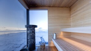 Eine Sauna mit Holzvertäfelung, einer Steinsäule und Blick auf eine verschneite Landschaft.