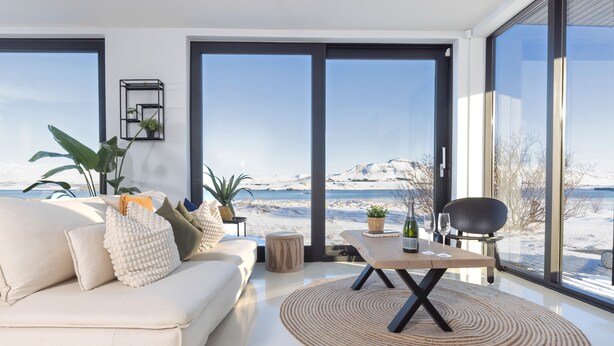 Ein modernes Wohnzimmer mit einer Couch, einem Couchtisch und großen Fenstern mit Blick auf eine verschneite Landschaft.