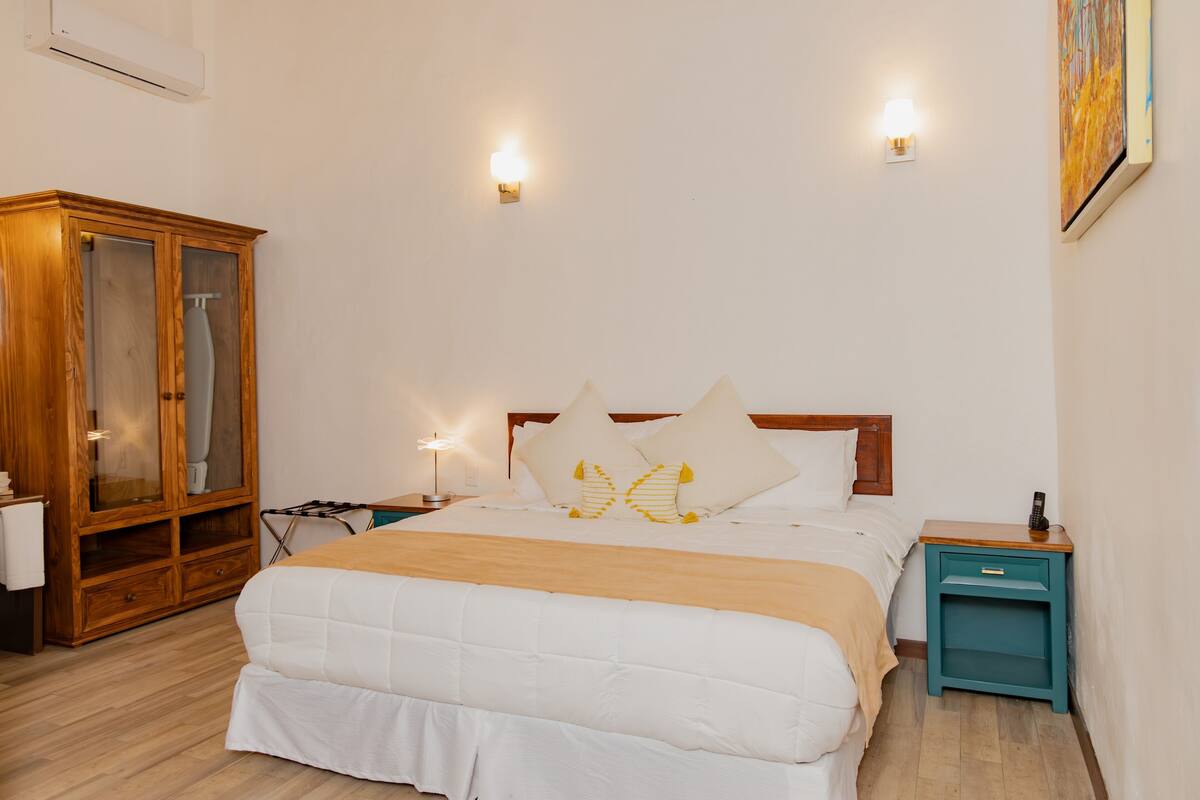 A neatly arranged bedroom with a bed, a wooden wardrobe, bedside tables, and wall-mounted lights.