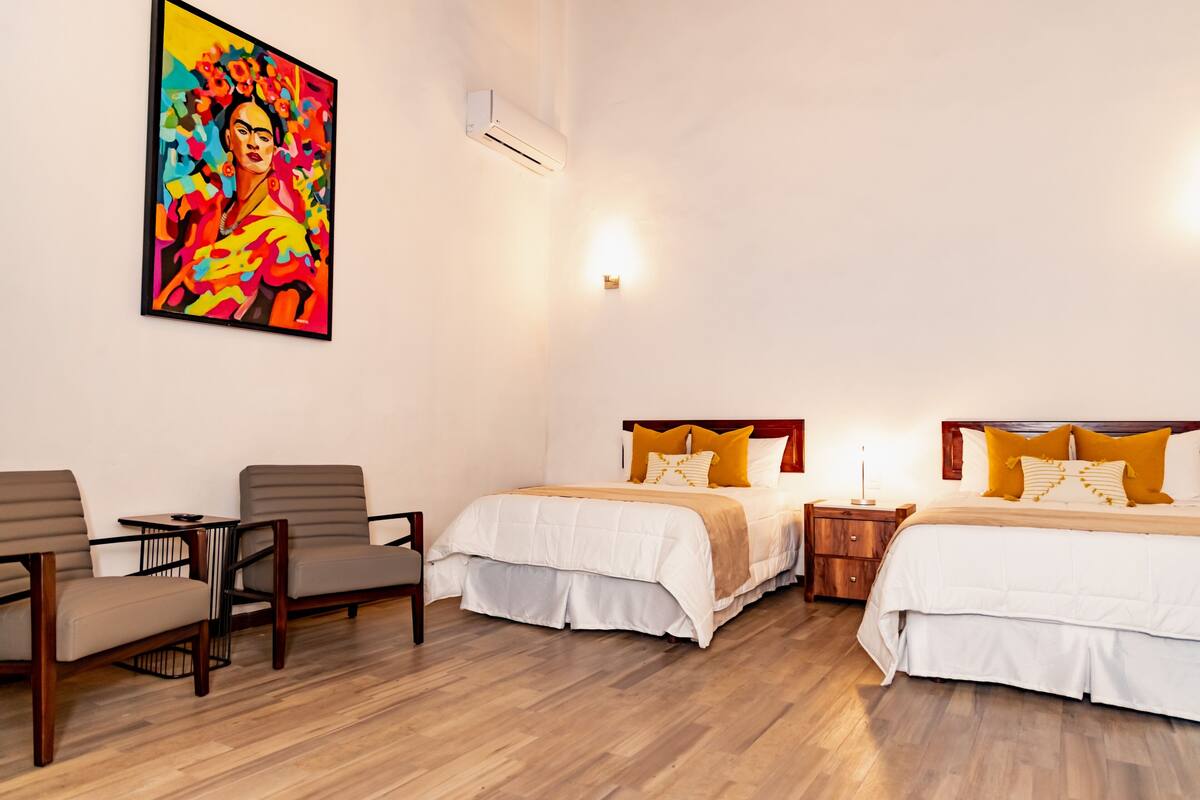 A hotel room with two beds, a painting on the wall, a small table, and a chair.