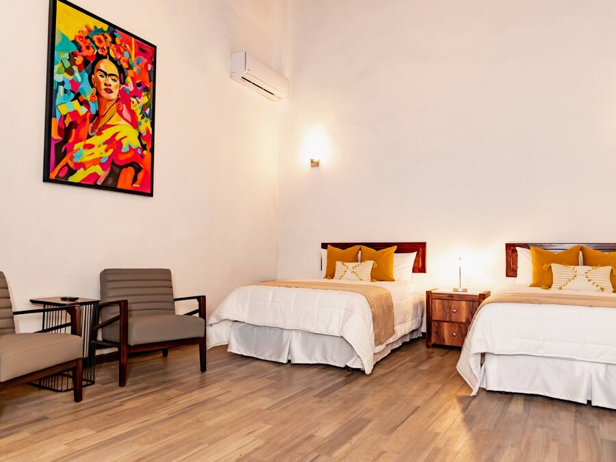 Habitación de hotel con dos camas, un cuadro en la pared, una mesita y una silla.
