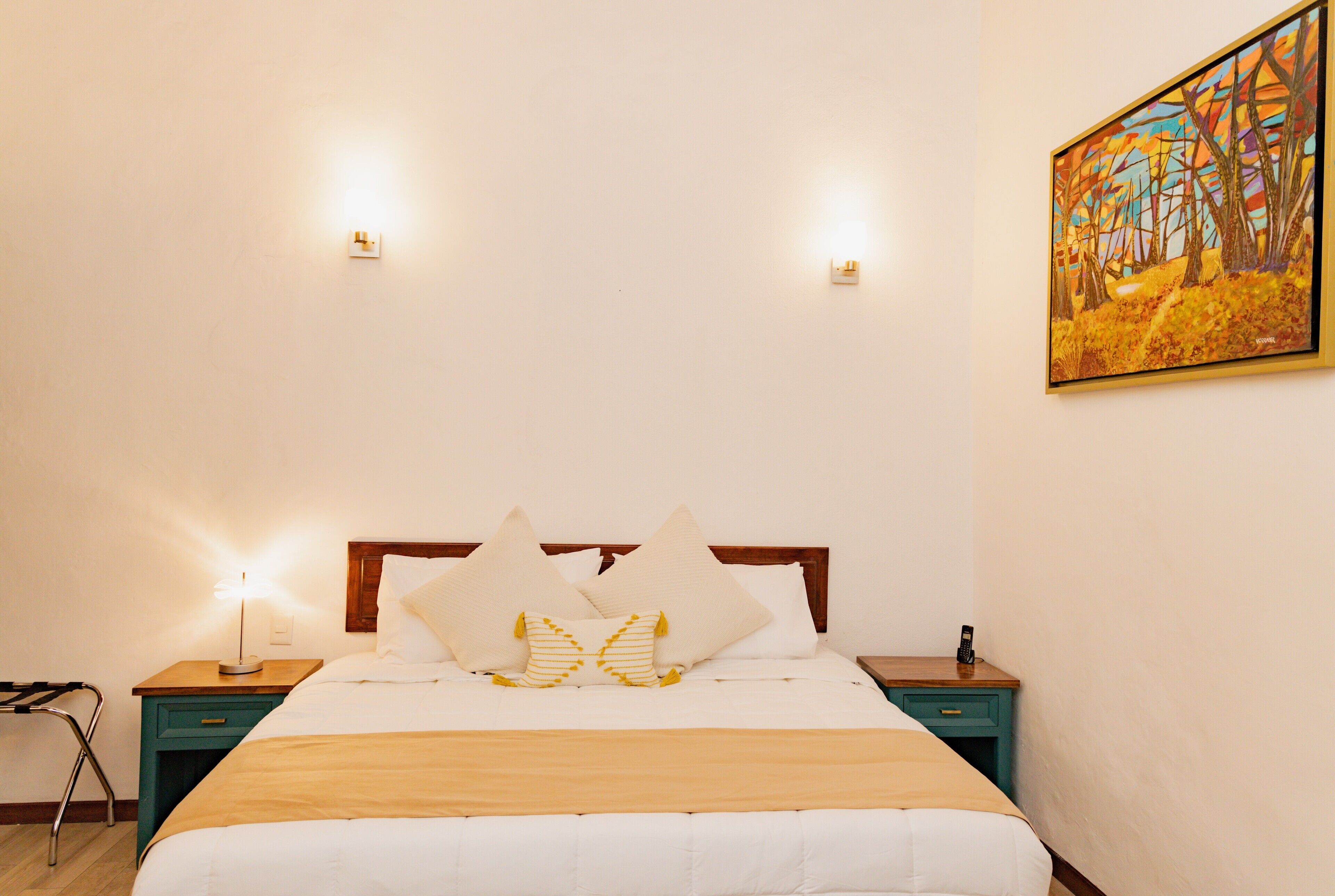 A neatly made bed with white and yellow pillows, a wooden headboard, and a bedside table with a lamp.
