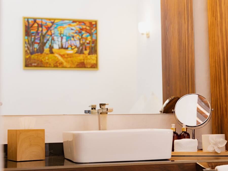 A bathroom with a white sink, a mirror, a wooden cutting board, a towel, and a bottle of lotion.