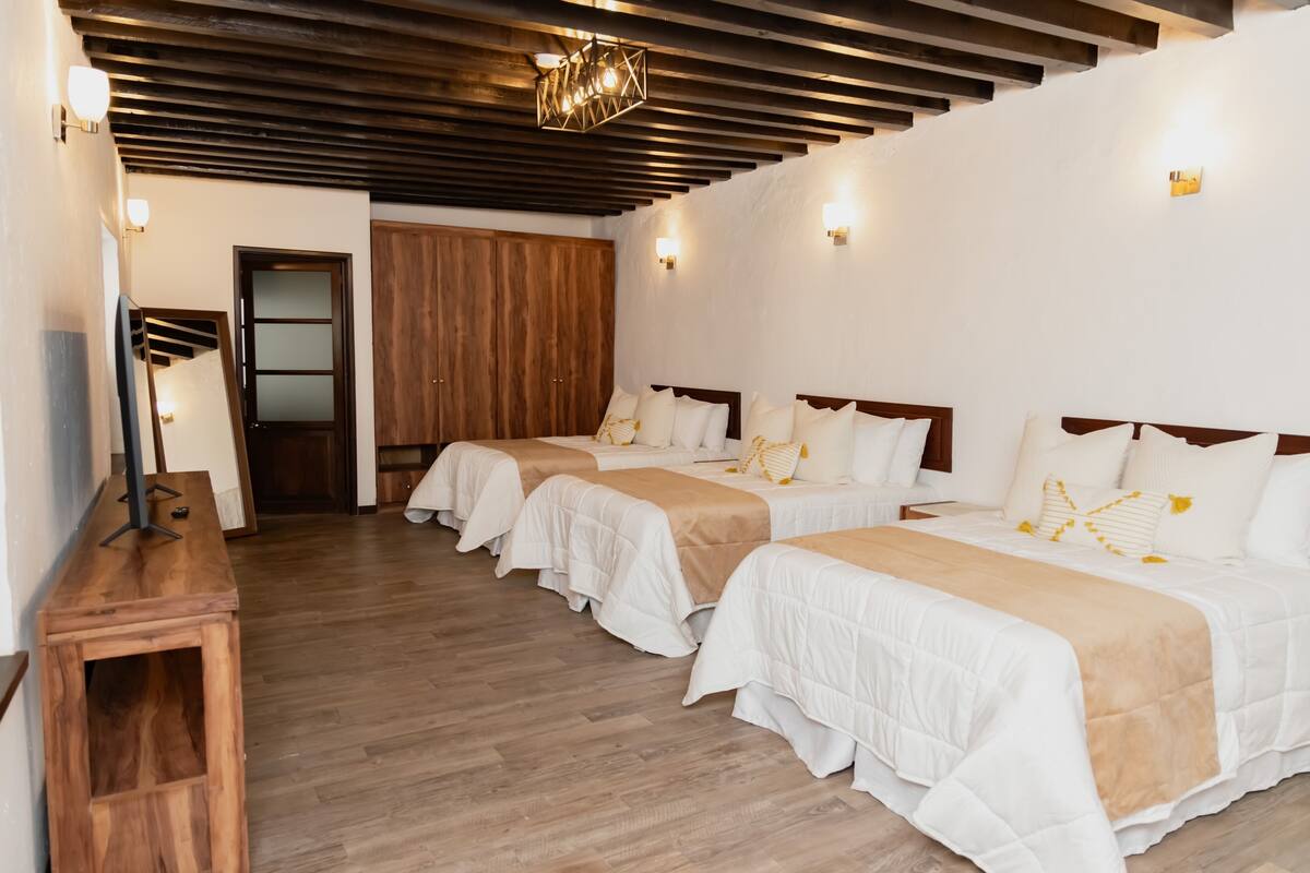 A hotel room with three beds, wooden flooring, and a modern chandelier.