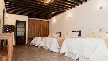 A hotel room with wooden flooring, a bed with white bedding, a wooden wardrobe, and a ceiling with exposed beams.