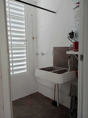 Um banheiro pequeno com pia branca, janela com persianas e porta.