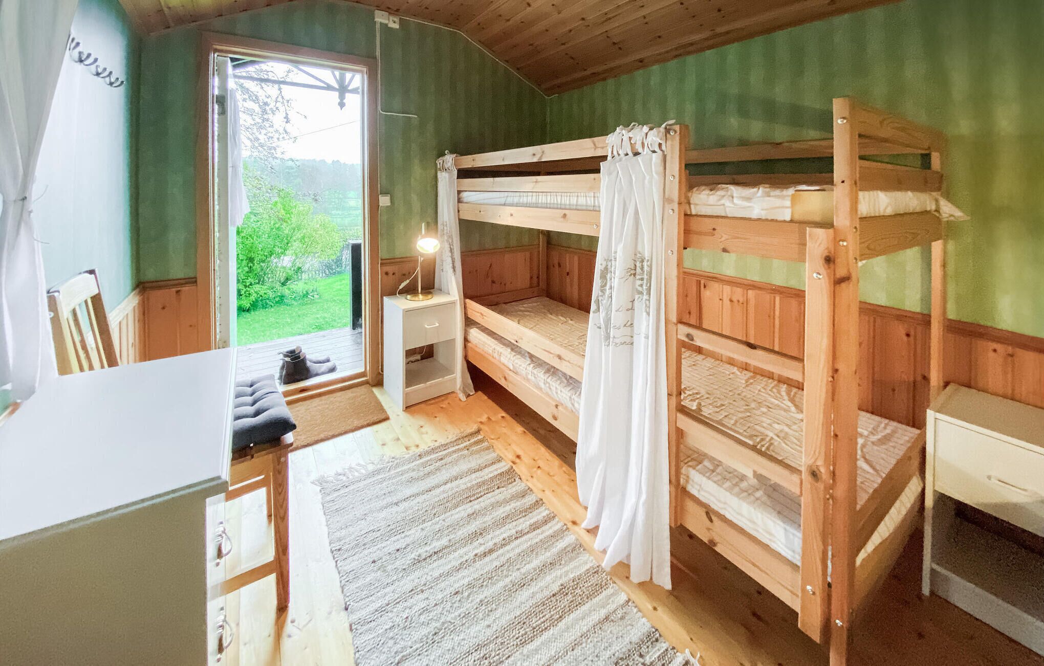 A bunk bed room with a desk and chair, a small table, and a window with a view of greenery.