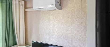 Een kamer met een bed, een televisie, een airconditioner en een raam met gordijnen.