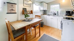 Una cocina compacta con armarios blancos, una mesa de comedor de madera y un ventanal pequeño.