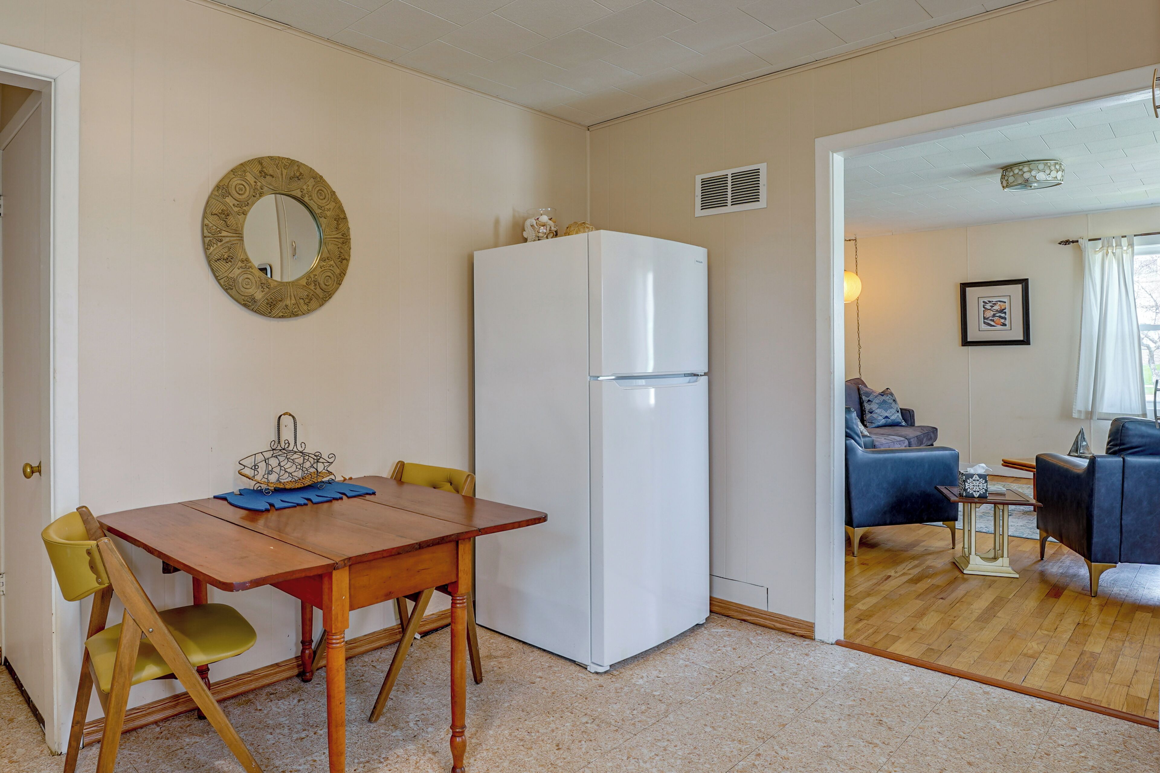 Un espace de vie compact comprenant un coin repas, un réfrigérateur blanc et un coin salon avec un canapé et des fauteuils.