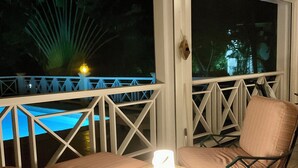 Un balcone con mobili in vimini, un tavolo con una luce e vista su una piscina di notte.