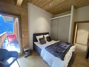 Une chambre à coucher comprenant un lit, une chaise, une petite table et une porte coulissante donnant sur un balcon.