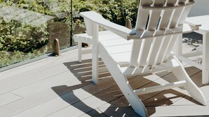 A white Adirondack chair on a wooden deck overlooking a garden with a view of the ocean. - White House (Byron Bay)