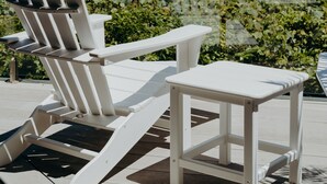 A white Adirondack chair and a small table on a wooden deck overlooking a beach with waves and distant mountains. - White House (Byron Bay)
