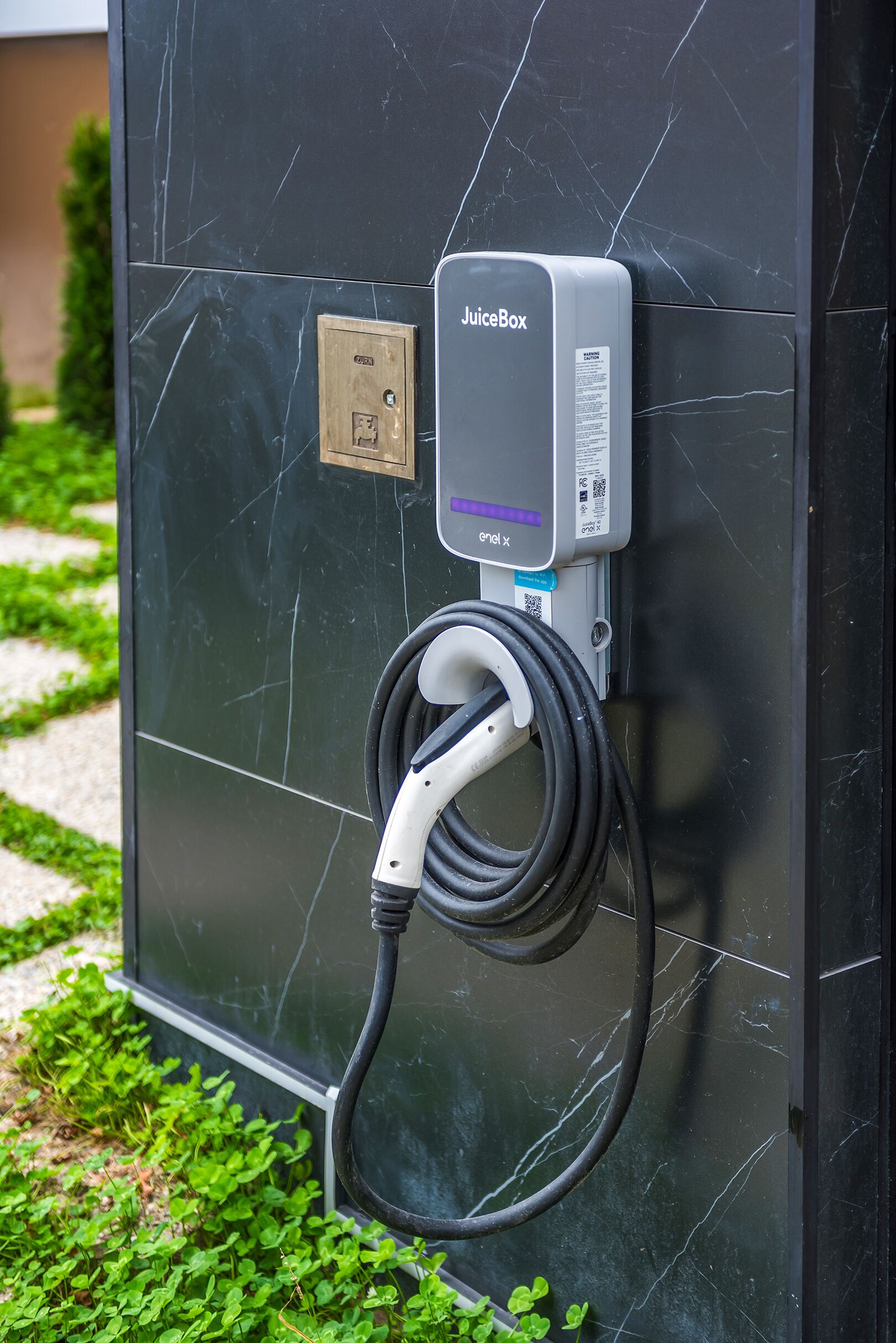 Une borne de recharge JuiceBox fixée à un mur en marbre foncé.