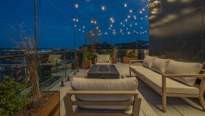 Een terras op het dak, ingericht met een bank, stoelen, een salontafel en verlicht met lichtslingers.