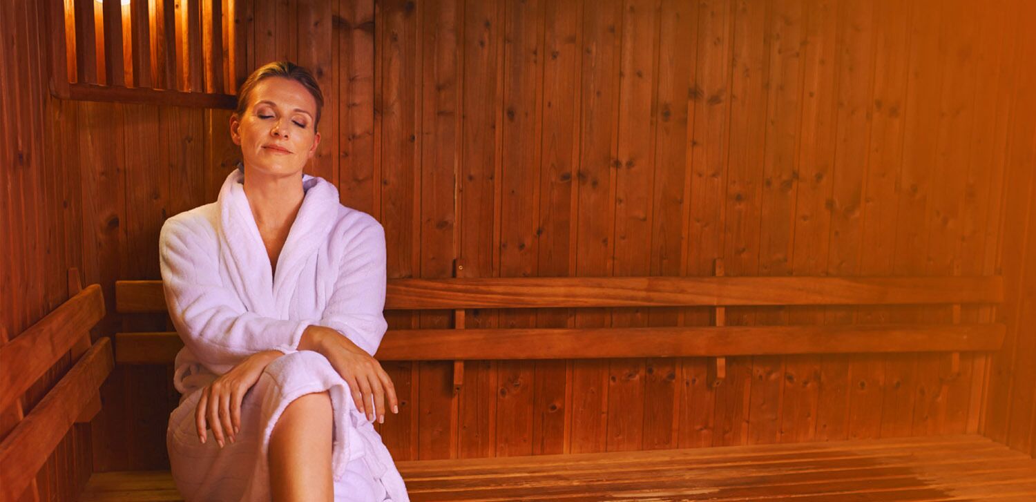 Iemand zit in een houten sauna met banken en een houten wand.