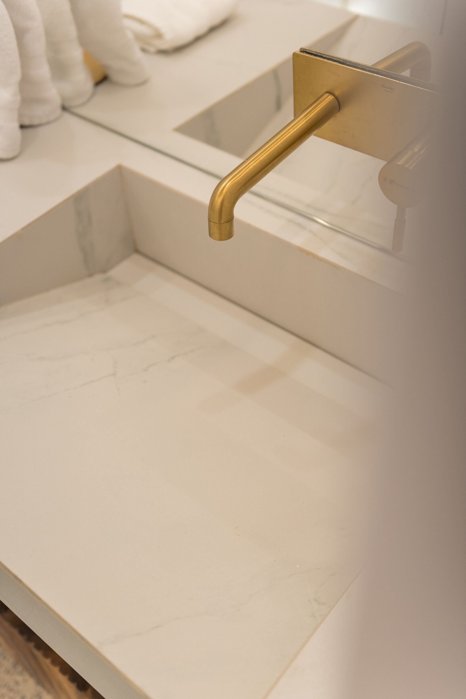Un baño con lavamanos de mármol blanco, grifo dorado y toallero.