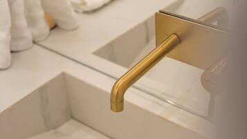 A bathroom with a white marble sink, gold faucet, and a towel rack.