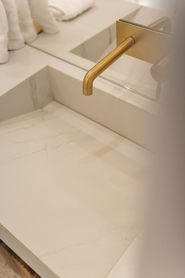 A bathroom with a white marble sink, gold faucet, and a towel rack.
