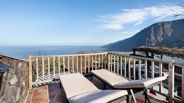 A terrace with two lounge chairs, a stone wall, and a view of the sea and mountains. - Chalet 'La Higuera' with Sea View, Shared Terrace and Wi-Fi (Frontera)
