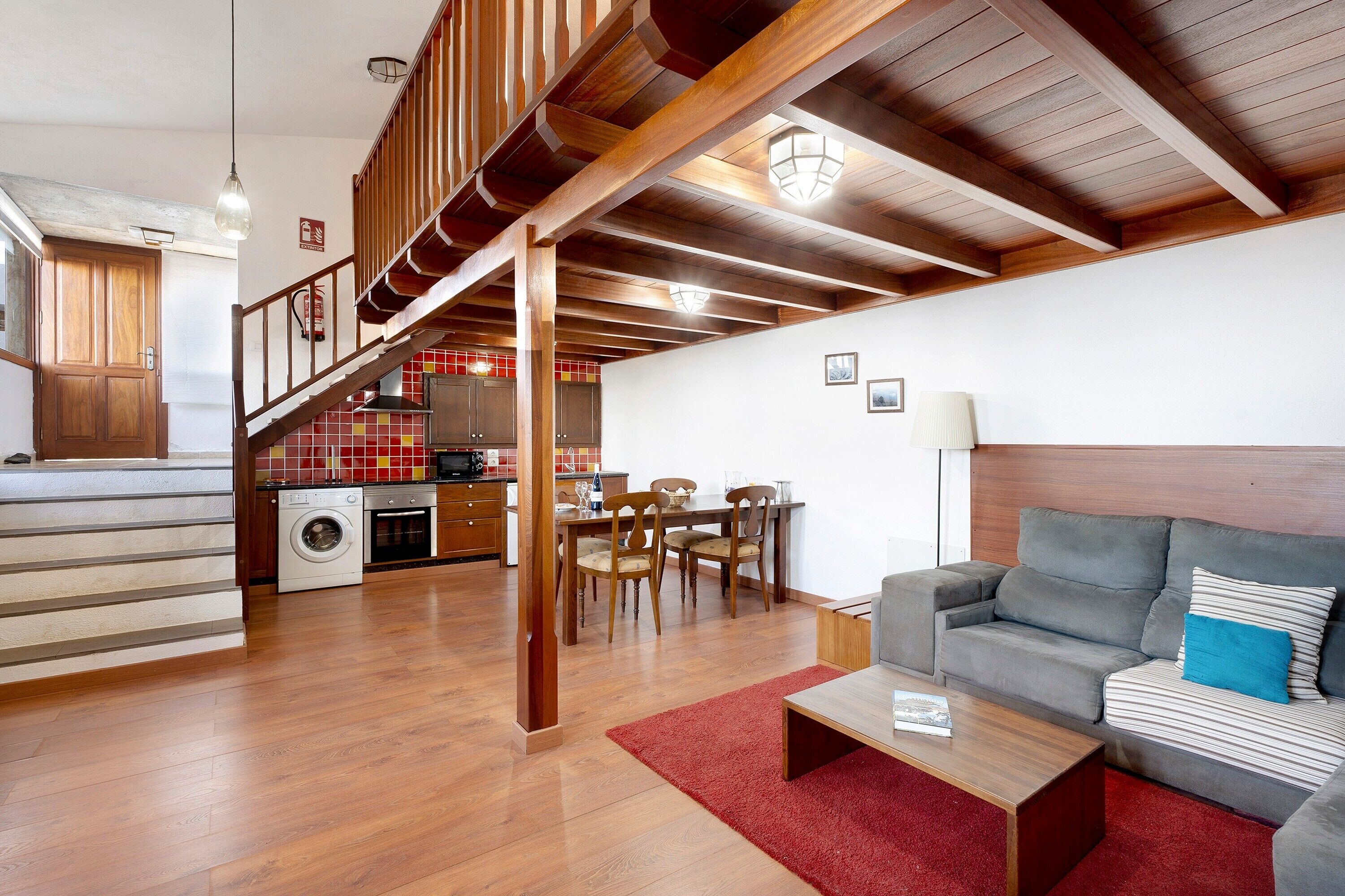 Ein geräumiger Wohnbereich mit einer Couch, einem Couchtisch und einem Esstisch mit Stühlen. Eine Treppe führt zu einer oberen Ebene.