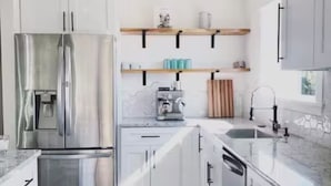 A modern kitchen with white cabinets, a stainless steel refrigerator, a coffee machine, and a water dispenser. - E+H House-Views! Fast Wifi & Pet friendly! (Lyle)