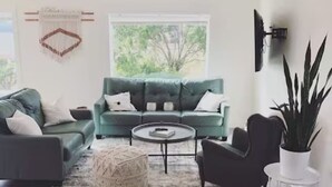 A modern living room with a teal sofa, a round coffee table, and a large potted plant. - E+H House-Views! Fast Wifi & Pet friendly! (Lyle)