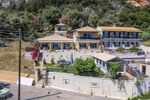 A multi-story building with balconies, a swimming pool, and a view of a mountainous area. - Studio Apartment 'Angela 2' with Sea View, Wi-Fi and Air Conditioning (Corfu)