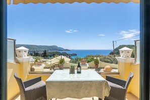 Een balkon met een tafel, stoelen, plantenbakken en uitzicht op zee.