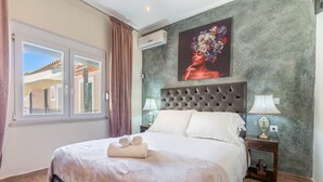 Un dormitorio con una cama grande, dos mesitas de noche con lámparas, aire acondicionado instalado en la pared y una ventana con cortinas.