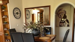 Un comedor con una mesa de madera, sillas negras, un jarrón con plantas, un reloj y una obra de arte enmarcada.