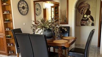 A dining area with a wooden table, black chairs, a vase with plants, a clock, and a framed artwork.