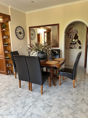 Un coin repas avec une table en bois, des chaises noires, un vase avec des plantes, une horloge et une œuvre d’art encadrée.