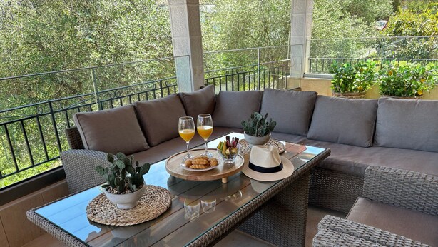 Un patio soleado con muebles de mimbre, una mesa de vidrio y vistas al verdor.
