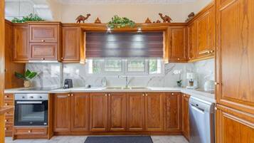 Una cocina con armarios de madera, encimera de mármol, horno empotrado, lavavajillas y ventana con vistas a la vegetación.