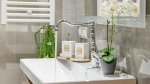 Un baño con un lavamanos blanco, un perchero para toallas, una planta en maceta y dos botellas etiquetadas 'BATH'.