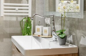 A bathroom with a white sink, a towel rack, a potted plant, and two bottles labeled 'BATH'.