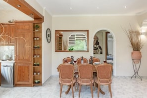 A dining area with a wooden cabinet, a dining table with chairs, a clock, and a potted plant.