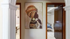 Un pasillo con una obra de arte enmarcada que muestra a una persona vestida con traje tradicional, una cama y una puerta de madera.