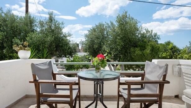 Een balkon met twee houten stoelen, een klein rond tafeltje en een bloeiende plant in een pot.