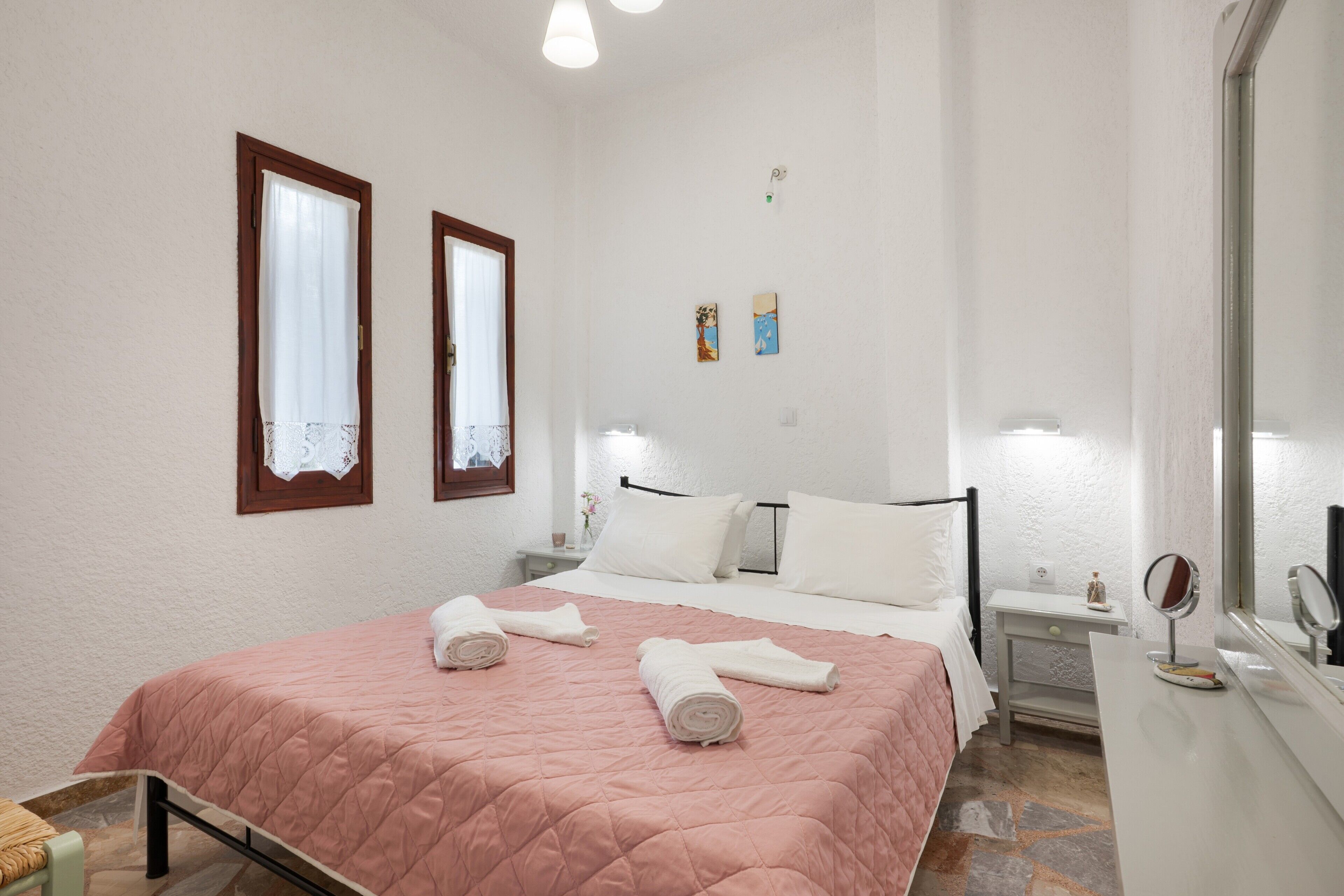 Een slaapkamer met een bed, nachtkastjes, een spiegel en een raam met gordijnen.